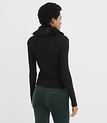 A woman wearing a black ribbed top with a faux-fur collar and dark green trousers stands against a plain white background. carousel Product Image 3
