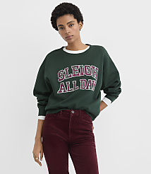A woman wearing a green "SLEIGH ALL DAY" sweatshirt and burgundy corduroy pants stands against a plain white background. carousel Product Image 1