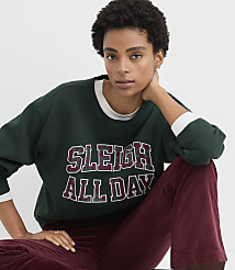 A woman wearing a dark green "SLEIGH ALL DAY" sweatshirt and maroon corduroy pants poses against a plain white background. carousel Product Image 2