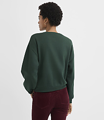 A woman with curly hair wearing a dark green sweatshirt and maroon corduroy pants stands against a plain white background. carousel Product Image 3