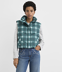 A woman wearing a green plaid puffer vest, a grey speckled sweater, and embellished blue jeans stands against a plain white background. carousel Product Image 1