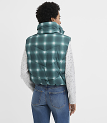 A woman wearing a green plaid puffer vest, a speckled white long-sleeve shirt, and blue jeans stands against a plain white background. carousel Product Image 3