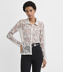 A woman wearing a sheer white lace button-down shirt and black trousers stands against a plain white background. carousel Product Image 1