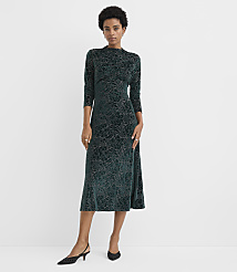 A woman wearing a dark green floral velvet dress and black heels stands against a plain white background. carousel Product Image 1