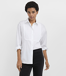 A woman wearing a white pleated button-down shirt and black trousers stands against a plain white background. carousel Product Image 2