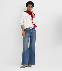 A woman wearing a white "Merry" sweatshirt, a red scarf, and wide-leg blue jeans stands against a plain white background. carousel Product Image 3