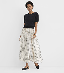 A woman wearing a black short-sleeved top and a long white polka-dot skirt stands against a plain white background. carousel Product Image 1