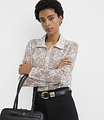 A woman wearing a floral lace blouse and black trousers stands with her arms crossed against a plain white background. carousel Product Image 2