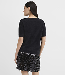 A woman wearing a fuzzy black short-sleeved top and a sequined black skirt stands with her back to the camera against a plain light gray background. carousel Product Image 3