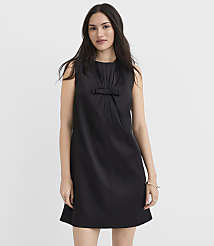 A woman wearing a sleeveless black dress with a bow detail stands against a plain white background. carousel Product Image 2