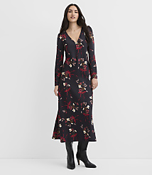 A woman wearing a long-sleeved black floral dress and black boots stands against a plain white background. carousel Product Image 1