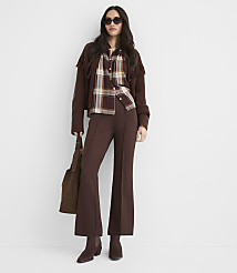 A woman in a brown plaid shirt, cropped jacket with fringe, and flared pants stands against a plain white background, holding a brown suede bag. carousel Product Image 1