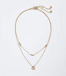 A layered gold necklace with small sparkling crystals rests against a plain white background. carousel Product Image 1