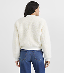 A woman wearing a white fuzzy jacket and blue jeans stands with her back to the camera against a plain light gray background. carousel Product Image 3