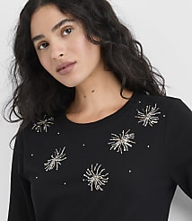 A woman with long, wavy dark hair wearing a black shirt with silver and gold sequin starbursts poses against a plain white background. carousel Product Image 1