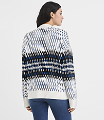 A woman wearing a patterned white, blue, and black sweater and blue jeans stands against a plain white background. carousel Product Image 4