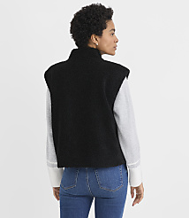 A woman wearing a black fleece vest over a grey long-sleeved shirt and blue jeans stands against a plain white background. carousel Product Image 3