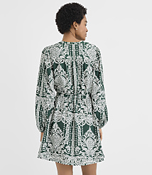 A woman wearing a green and white patterned dress stands with her back to the camera against a plain white background. carousel Product Image 3