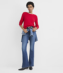 A woman wearing a red sweater and flared blue jeans stands against a plain white background. carousel Product Image 2