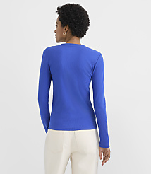 A woman wearing a bright blue long-sleeved shirt and white pants stands with her back to the camera against a plain white background. carousel Product Image 3