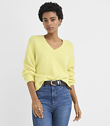 A woman wearing a yellow V-neck sweater and blue jeans stands against a plain white background. carousel Product Image 1