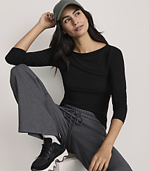 A woman wearing a black long-sleeved shirt, grey joggers, and a green cap poses against a plain, light-colored background. carousel Product Image 2