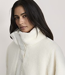 A woman with long dark hair wearing a white fuzzy jacket stands against a plain, light-colored background. carousel Product Image 4