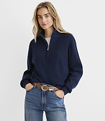 A blonde woman wearing a navy blue quarter-zip sweater and blue jeans stands against a plain white background. carousel Product Image 1
