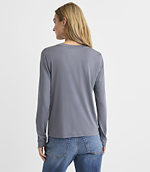 A woman with blonde hair wearing a grey long-sleeved shirt and blue jeans stands against a plain white background. carousel Product Image 3