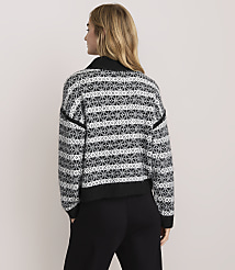 A woman with blonde hair wearing a patterned black and white sweater and black pants stands against a plain light-colored background. carousel Product Image 3