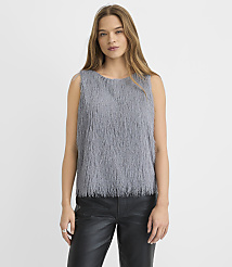 A woman wearing a grey shaggy sleeveless top and black leather pants stands against a plain white background.