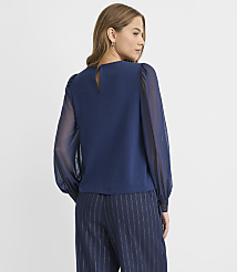 A woman wearing a navy blue blouse with sheer sleeves and pinstriped trousers stands against a plain white background. carousel Product Image 3
