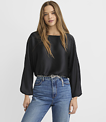 A woman wearing a black satin blouse and blue jeans stands against a plain white background. carousel Product Image 2