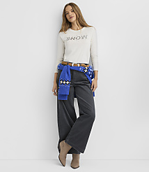 A woman wearing a white "SNOW" shirt, wide-leg dark trousers, and a blue sweater tied around her waist stands against a plain white background. carousel Product Image 3