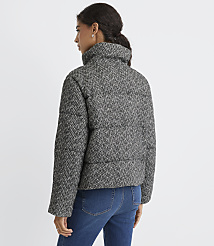 A woman wearing a black and white herringbone puffer jacket and blue jeans stands against a plain white background. carousel Product Image 3