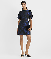 A woman wearing a navy blue floral puff-sleeve dress and black heels stands against a plain white background. carousel Product Image 1