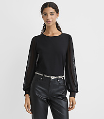 A woman wearing a black top with sheer sleeves and black faux-leather pants stands against a plain white background. carousel Product Image 1