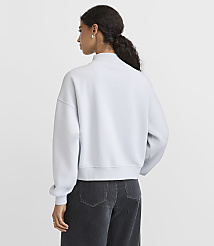 A woman wearing a light blue sweatshirt and dark corduroy pants stands with her back to the camera against a plain white background. carousel Product Image 3