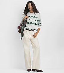 A woman wearing a patterned white and green sweater and wide-leg cream pants stands against a plain white background. carousel Product Image 2