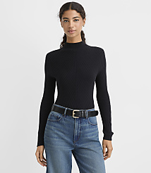 A woman wearing a black ribbed mock-neck sweater, blue jeans, and a black belt stands against a plain light gray background. carousel Product Image 1
