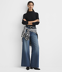 A woman wearing a black ribbed top, wide-leg jeans, and a checkered shirt tied around her waist stands against a plain white background. carousel Product Image 2
