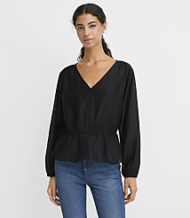 A woman wearing a black long-sleeved blouse and blue jeans stands against a plain white background. carousel Product Image 1