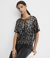 A woman wearing a sequined black top and leather pants sits against a plain white background. carousel Product Image 1