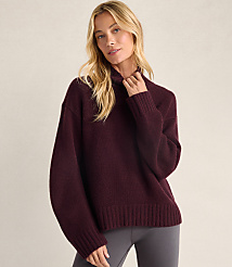 A blonde woman wearing a maroon oversized sweater and grey leggings stands against a plain, light-colored background. carousel Product Image 1