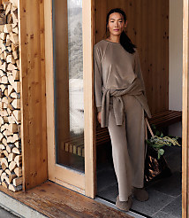 A woman in a taupe lounge set stands in a wooden doorway, with a stack of firewood to her left and a rustic interior behind her. carousel Product Image 3