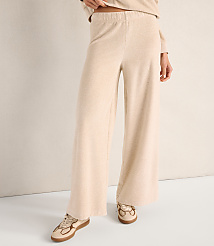 A person wears wide-leg beige trousers and matching sneakers against a plain, neutral-toned wall and floor. carousel Product Image 2
