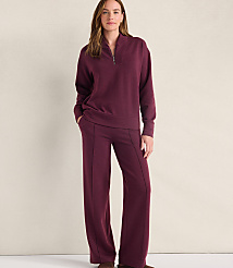 A woman wearing a maroon quarter-zip pullover and matching wide-leg pants stands against a plain, light-colored wall. carousel Product Image 1