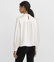 A woman wearing a cream-colored satin blouse and black trousers stands with her back to the camera against a plain light gray background. carousel Product Image 3