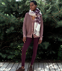 A woman wearing a mauve cardigan, burgundy leggings, and a patterned scarf stands on a wooden deck against a backdrop of dense evergreen trees. carousel Product Image 3