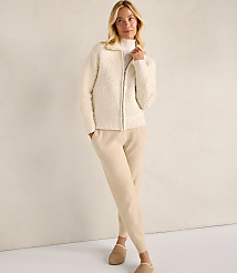 A woman wearing a cream-colored textured zip-up jacket and matching pants stands against a plain, neutral-toned wall. carousel Product Image 2